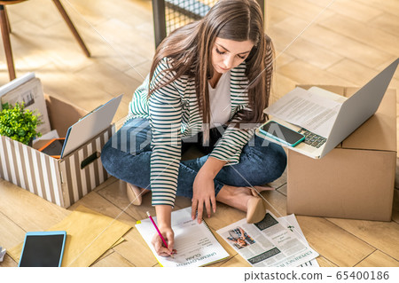 Young woman sitting on the floor and filling application Young woman sitting on the floor and filling application 65400186