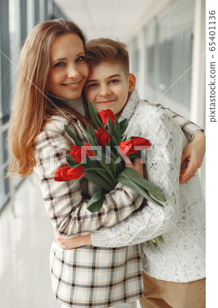 Son giving a mother a bunch of red tulips in amodern hall 65401136