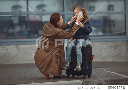 A European mother in a respirator with her daughter are standing near a building.The parent is teaching her child how to wear protective mask to save herself from virus 65401238