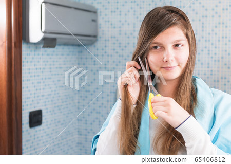 A beautiful young girl is holding a scissor to cut her hair herself during lockdown of coronavirus A beautiful young girl is holding a scissor to cut her hair herself during lockdown of coronavirus 65406812