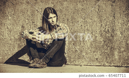 Man long haired sitting alone sad on grunge wall Man long haired sitting alone sad on grunge wall 65407711