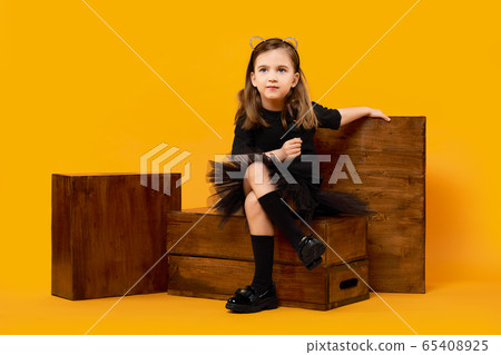 Young girl sitting among wooden apple boxes on orange background 65408925