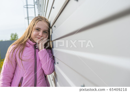 Beautiful teenager girl in a pink jacket leaning against the wall. Beautiful teenager girl in a pink jacket leaning against the wall. 65409218
