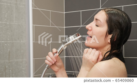 joyful young woman with wet hair sings into silver shower joyful young woman with wet hair sings into silver shower 65409860