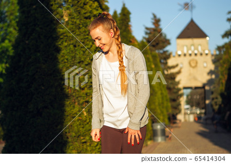 Young female runner, athlete resting after jogging in the city street in sunshine. Beautiful caucasian woman training, listening to music 65414304