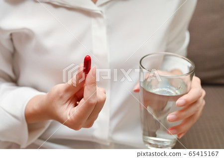 Close up Asian woman holding pill and a glass of water sitting on sofa Close up Asian woman holding pill and a glass of water sitting on sofa 65415167