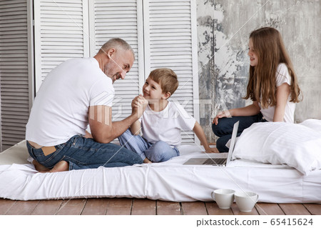 Father and son fight in their arms, and his daughter watches them. They are home on self-isolation. Father and son fight in their arms, and his daughter watches them. They are home on self-isolation. 65415624