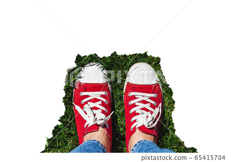 Legs in old red sneakers on green grass. View from above. The concept of youth, spring and freedom Legs in old red sneakers on green grass. View from above. The concept of youth, spring and freedom 65415784