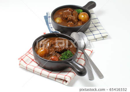 Beef stew on two black one-handed plates, with spoon, white background Beef stew on two black one-handed plates, with spoon, white background 65416332