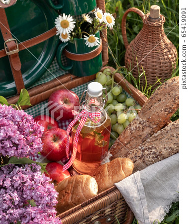 A bottle of water with fruit syrup and other food in a picnic basket, outdoors 65419091