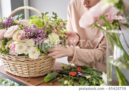 Floral shop concept . Florist woman creates flower arrangement in a wicker basket. Beautiful bouquet of mixed flowers. Handsome fresh bunch. Flowers delivery. 65428739