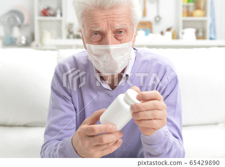 Portrait of sad sick senior man with facial mask holding pills Portrait of sad sick senior man with facial mask holding pills 65429890