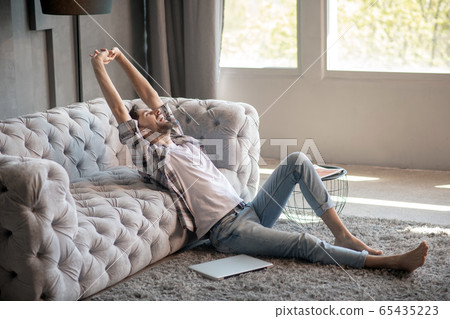 Bearded man sitting on the floor yawning stretching. 65435223