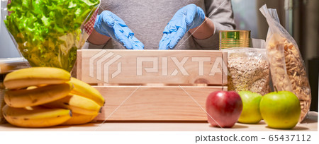 Volunteer hands in protective blue gloves showing in wooden box. Food donations concept. Focused on hands. Volunteer hands in protective blue gloves showing in wooden box. Food donations concept. Focused on hands. 65437112