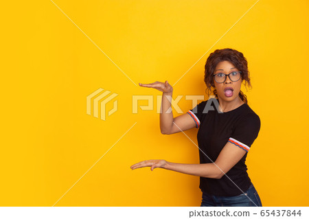 African-american beautiful young woman's portrait on yellow studio background, emotional and expressive. Copyspace for ad. African-american beautiful young woman's portrait on yellow studio background, emotional and expressive. Copyspace for ad. 65437844