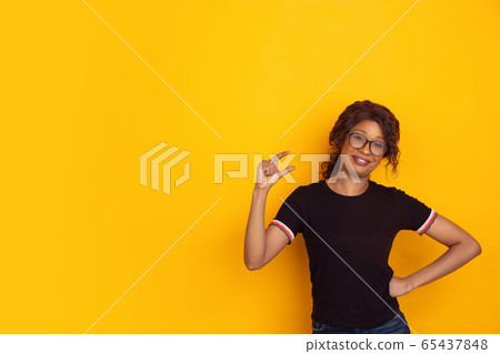 African-american beautiful young woman's portrait on yellow studio background, emotional and expressive. Copyspace for ad. African-american beautiful young woman's portrait on yellow studio background, emotional and expressive. Copyspace for ad. 65437848