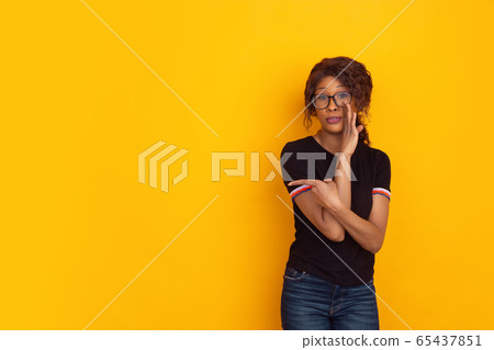 African-american beautiful young woman's portrait on yellow studio background, emotional and expressive. Copyspace for ad. African-american beautiful young woman's portrait on yellow studio background, emotional and expressive. Copyspace for ad. 65437851