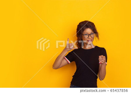 African-american beautiful young woman's portrait on yellow studio background, emotional and expressive. Copyspace for ad. 65437856