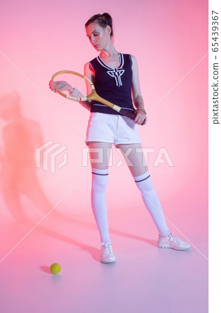 Girl tennis player with a racket in sportswear and white sneakers on a pink background in the Studio with shadow. Girl tennis player with a racket in sportswear and white sneakers on a pink background in the Studio with shadow. 65439367