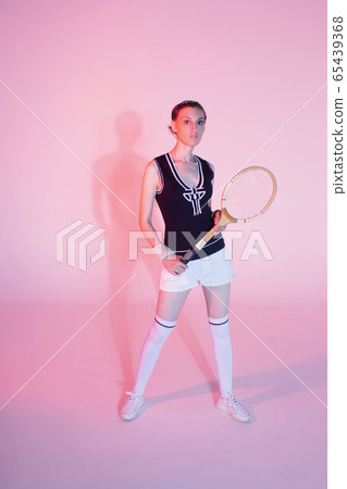 Girl tennis player with a racket in sportswear and white sneakers on a pink background in the Studio with shadow. Girl tennis player with a racket in sportswear and white sneakers on a pink background in the Studio with shadow. 65439368