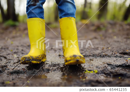 Mischievous preschooler child wearing yellow rain boots 65441235
