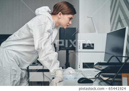 Beautiful young woman in protective suit using computer at work 65441924