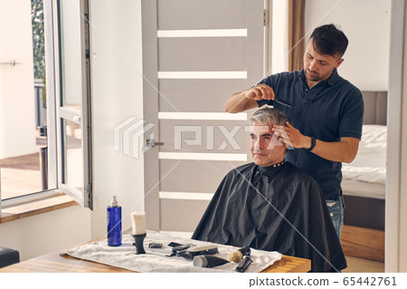 Handsome man cutting hair of mature client 65442761