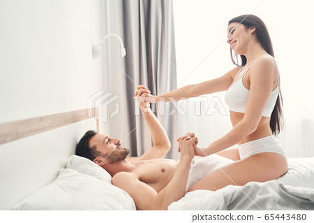 Newly wedded couple holding hands in bed 65443480