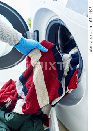 man putting clothes into the washing machine 65444024