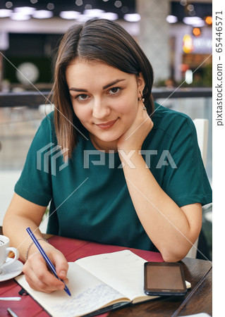 Young beautiful girl writes something in her notebook while sitting in the office Young beautiful girl writes something in her notebook while sitting in the office 65446571