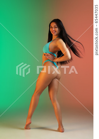 Fashion portrait of young fit and sportive woman in stylish blue luxury swimwear on gradient background. Perfect body ready for summertime. Fashion portrait of young fit and sportive woman in stylish blue luxury swimwear on gradient background. Perfect body ready for summertime. 65447035