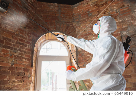 Coronavirus Pandemic. A disinfector in a protective suit and mask sprays disinfectants in the house or office 65449010