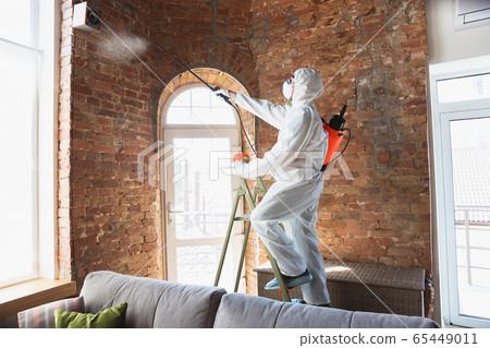 Coronavirus Pandemic. A disinfector in a protective suit and mask sprays disinfectants in the house or office Coronavirus Pandemic. A disinfector in a protective suit and mask sprays disinfectants in the house or office 65449011