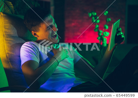 Cinematic portrait of handsome young man using devices, gadgets in neon lighted interior. Youth culture, bright colors 65449599