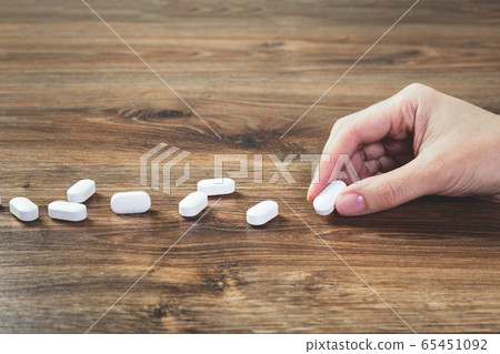 Hand with white tablets on wooden table. Medicine 65451092