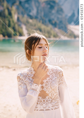 Beautiful bride in a white chiffon dress with sleeves and lace on the shore of Lake Lago di Braies in Italy. Destination wedding in Europe, on the popular Braies lake. 65458373