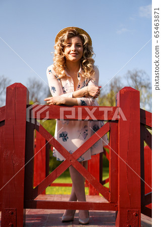 Beautiful woman in summer dress and straw hat stands on birch bridge in the park 65463871