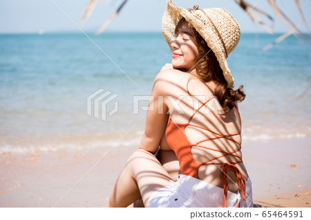A woman in a swimsuit sitting on the beach 65464591
