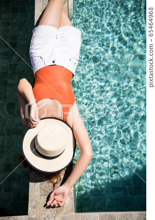 A woman in a swimsuit relaxing by the pool A woman in a swimsuit relaxing by the pool 65464968