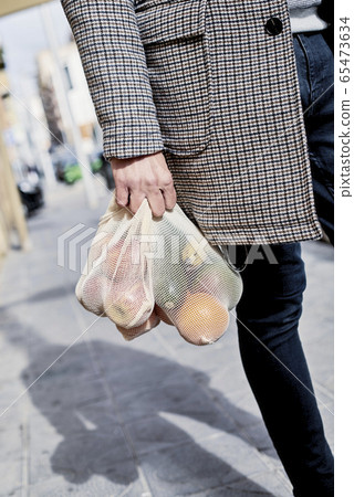 man carrying a mesh bag full of fruit and vegs 65473634