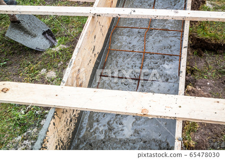 Steel rod reinforcement during pouring concrete into wooden frame 65478030