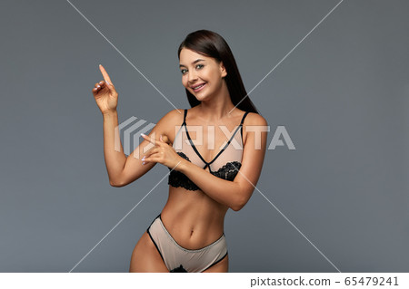 Portrait of a smiling fashion girl in a beautiful pear-shaped swimsuit pointing her finger at empty copy space. Copy space, gray background. Fashion concept Portrait of a smiling fashion girl in a beautiful pear-shaped swimsuit pointing her finger at empty copy space. Copy space, gray background. Fashion concept 65479241