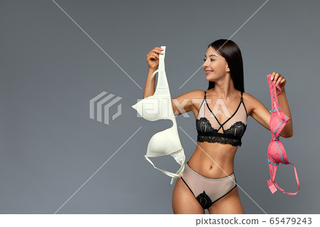 A difficult choice, a beautiful girl chooses a bra, holding bras of different colors in her hands. Gray background, copy space, make difficult choices. A difficult choice, a beautiful girl chooses a bra, holding bras of different colors in her hands. Gray background, copy space, make difficult choices. 65479243