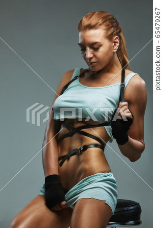Beautiful tanned red-haired girl dancer posing on a gray background in shorts and a t-shirt sexually posing. Beautiful female body dancing, training. Beautiful tanned red-haired girl dancer posing on a gray background in shorts and a t-shirt sexually posing. Beautiful female body dancing, training. 65479267