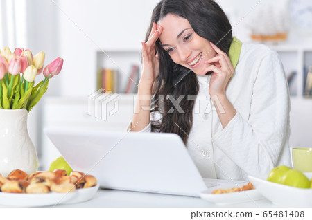 Beautiful young woman using laptop at table at home Beautiful young woman using laptop at table at home 65481408