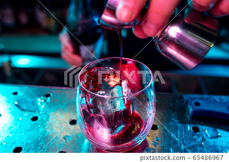 Close up of barman preparing of alcoholic cocktail with shot in multicolored neon light Close up of barman preparing of alcoholic cocktail with shot in multicolored neon light 65486967