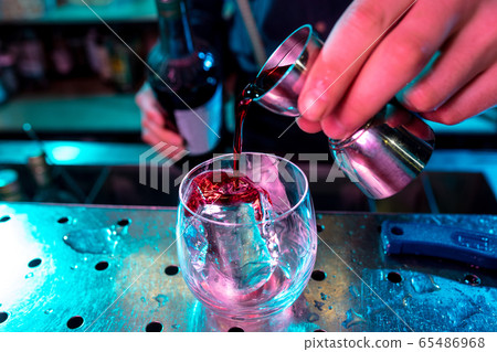 Close up of barman preparing of alcoholic cocktail with shot in multicolored neon light 65486968