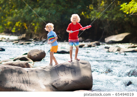 Child hiking in mountains. Kids at river shore. 65494019