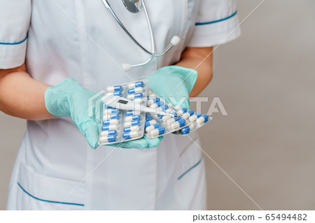 medical doctor nurse woman wearing protective mask and rubber or latex gloves - holding blisters of pills and thermometer medical doctor nurse woman wearing protective mask and rubber or latex gloves - holding blisters of pills and thermometer 65494482