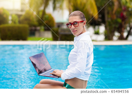 Woman with laptop at swimming pool. Remote work. 65494556